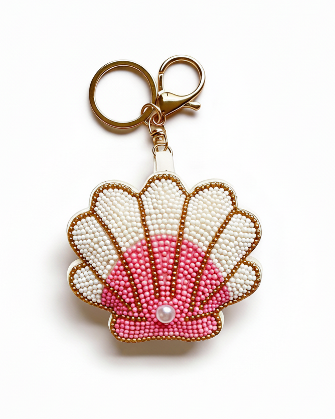 A seashell-shaped keychain bag made of white and pink seed beads with gold-tone metal trim and a lobster clasp, shown on a plain white background.