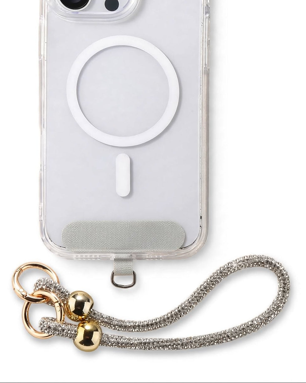 A clear protective phone case with a built-in white MagSafe ring, shown on a white iPhone. The case features a silver metallic mesh wrist strap attached at the bottom with gold-tone hardware.
