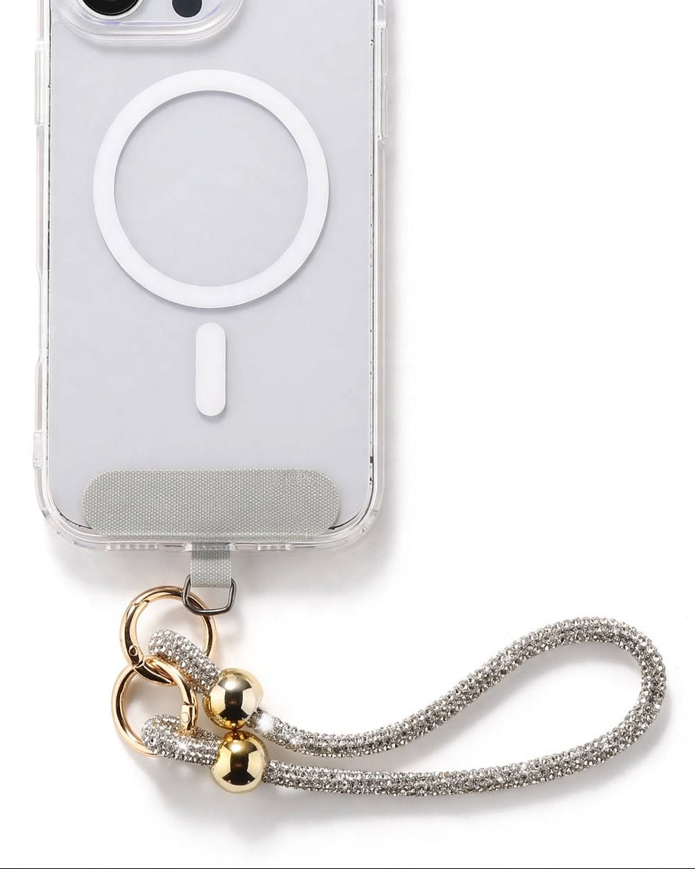 A clear protective phone case for an iPhone, featuring a white MagSafe ring on the back, a silver metallic strap, and gold-colored decorative beads.
