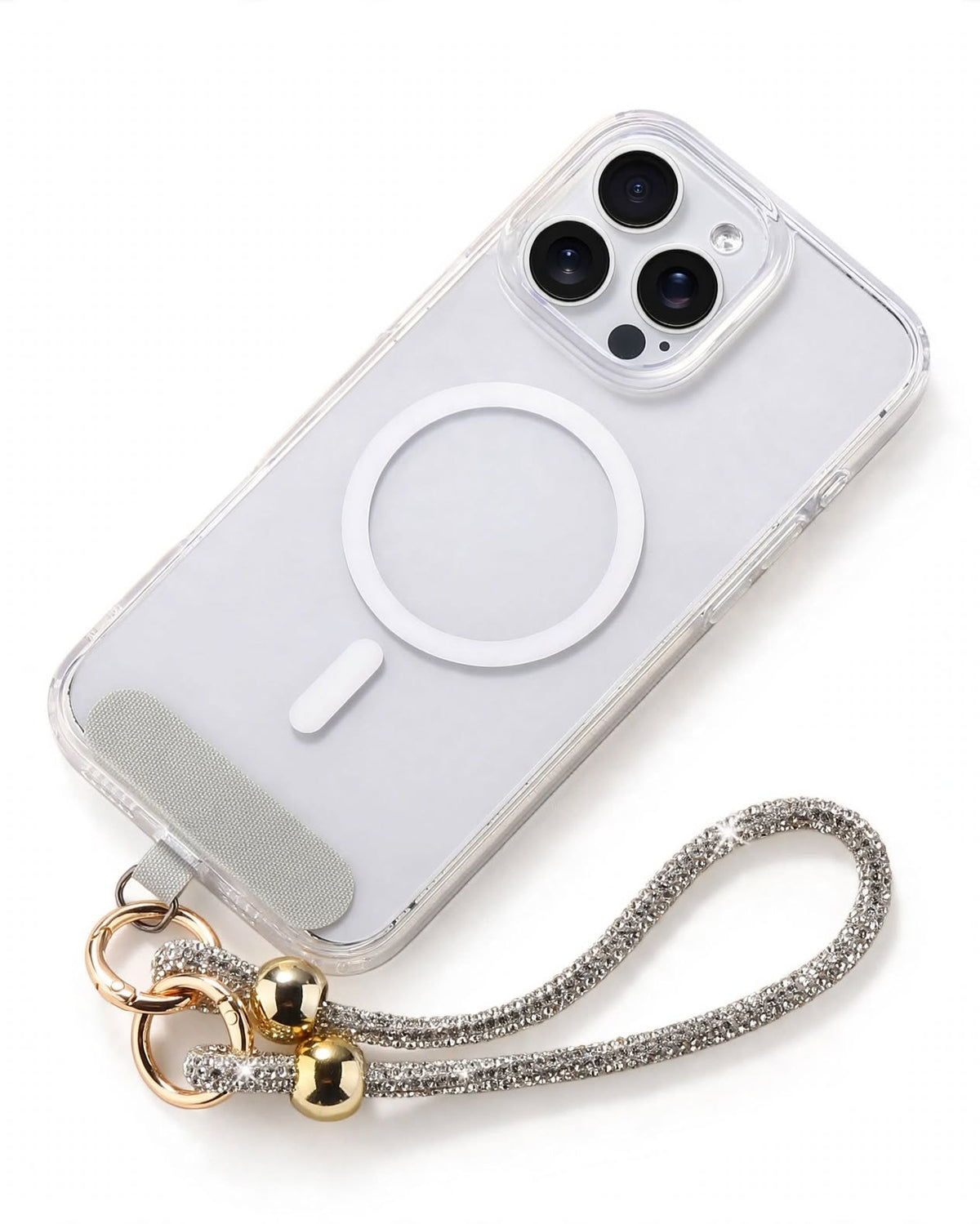 A clear protective phone case with a white MagSafe ring, shown on a white phone. The case is attached to a silver rhinestone-embellished wrist strap with gold-colored metal rings and beads, photographed on a clean white background.