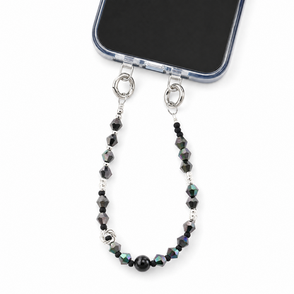A silver metal phone strap with faceted black beads and iridescent accents, attached to a smartphone on a clean white background.